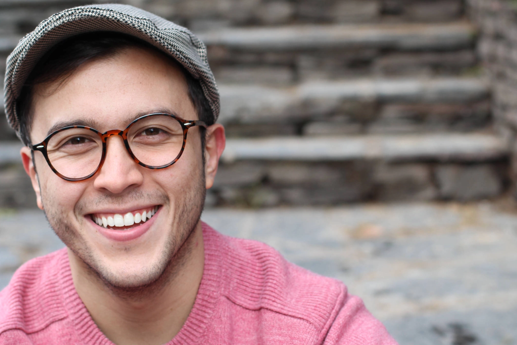 Ein junger Mann mit Mütze und Brille lächelt in die Kamera.