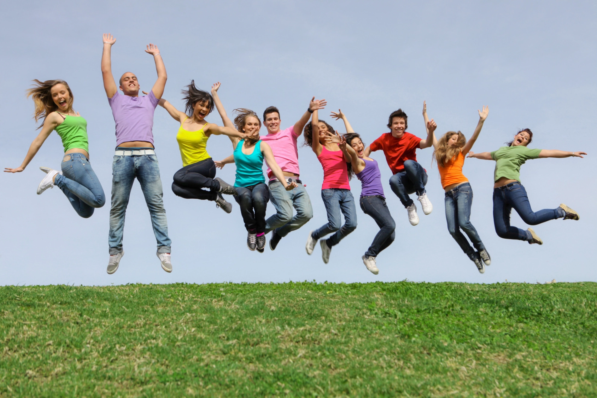 Menschen in bunten T-Shirts auf Wiese springen in die Luft